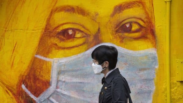 Una persona con una mascherina passa davanti a un murale che raffigura la stessa cosa nel distretto di Soho, a Hong Kong. Credit: Miguel Candela Poblacion : Anadolu Agency via Getty.